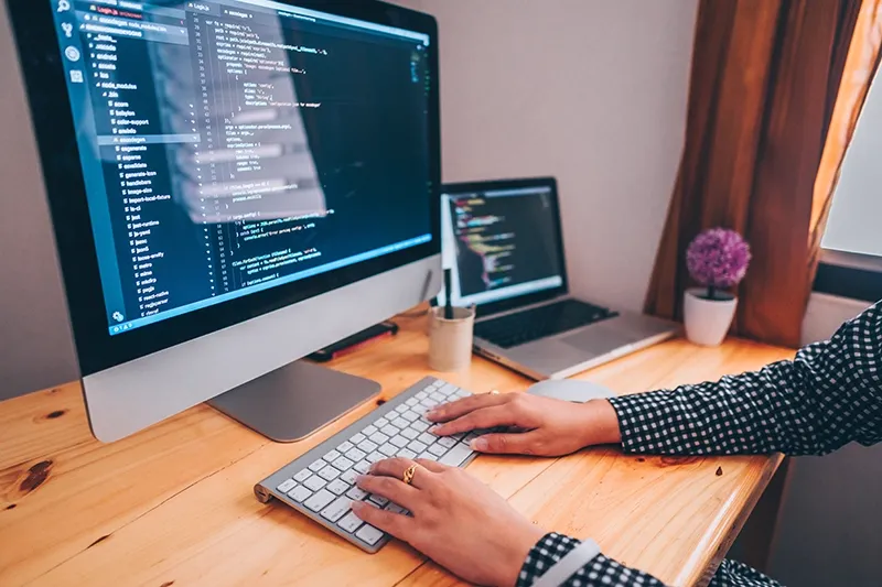 A web designer working on a custom affordable website project on a large desktop screen with code displayed.